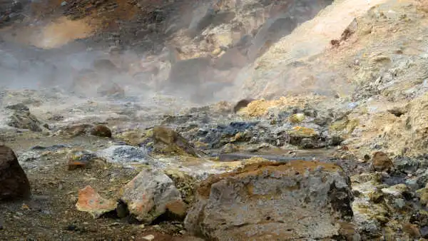 Sulfur-colored rocks can be seen behind a fog of natural steam